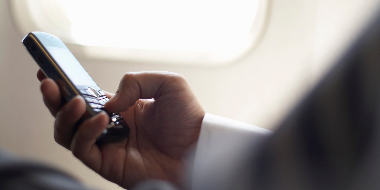 Close-up on hands of business man, sitting in airplane, holding mobile phone